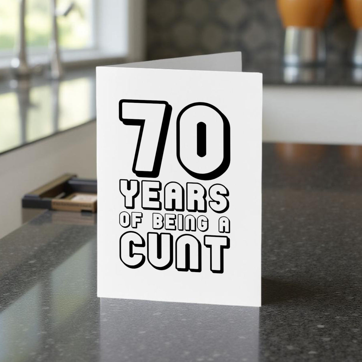 Birthday card with text '70 YEARS OF BEING A CUNT' on a kitchen counter.