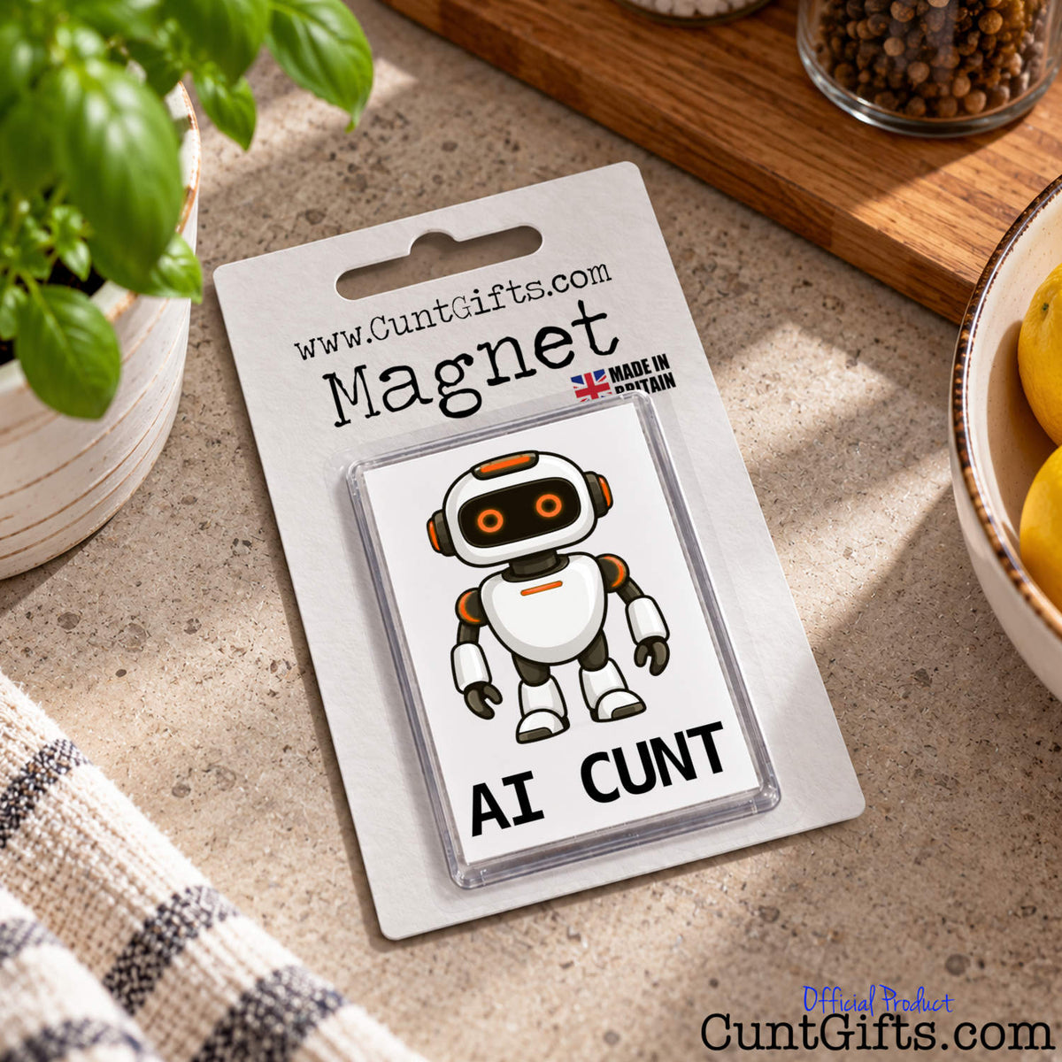 Packaged AI Cunt novelty fridge magnet featuring a cheeky robot design displayed on a kitchen worktop beside a striped tea towel.