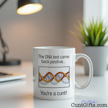 "The DNA Test - You're a cunt" - Mug on desk with plant and lamp