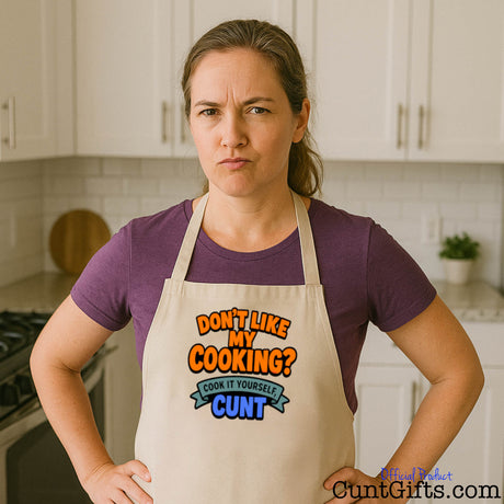 Stressed mum in kitchen wearing cooking apron that reads "Don't like my cooking? Cook it yourself cunt"