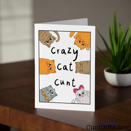 Crazy Cat Cunt Card on a wooden surface with a plant in the background