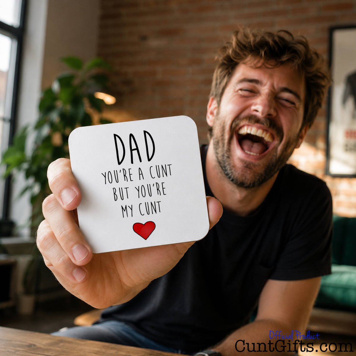 Dad You're a Cunt But You're My Cunt - Drink coaster held by man with beard laughing in office with brick wall and plant.