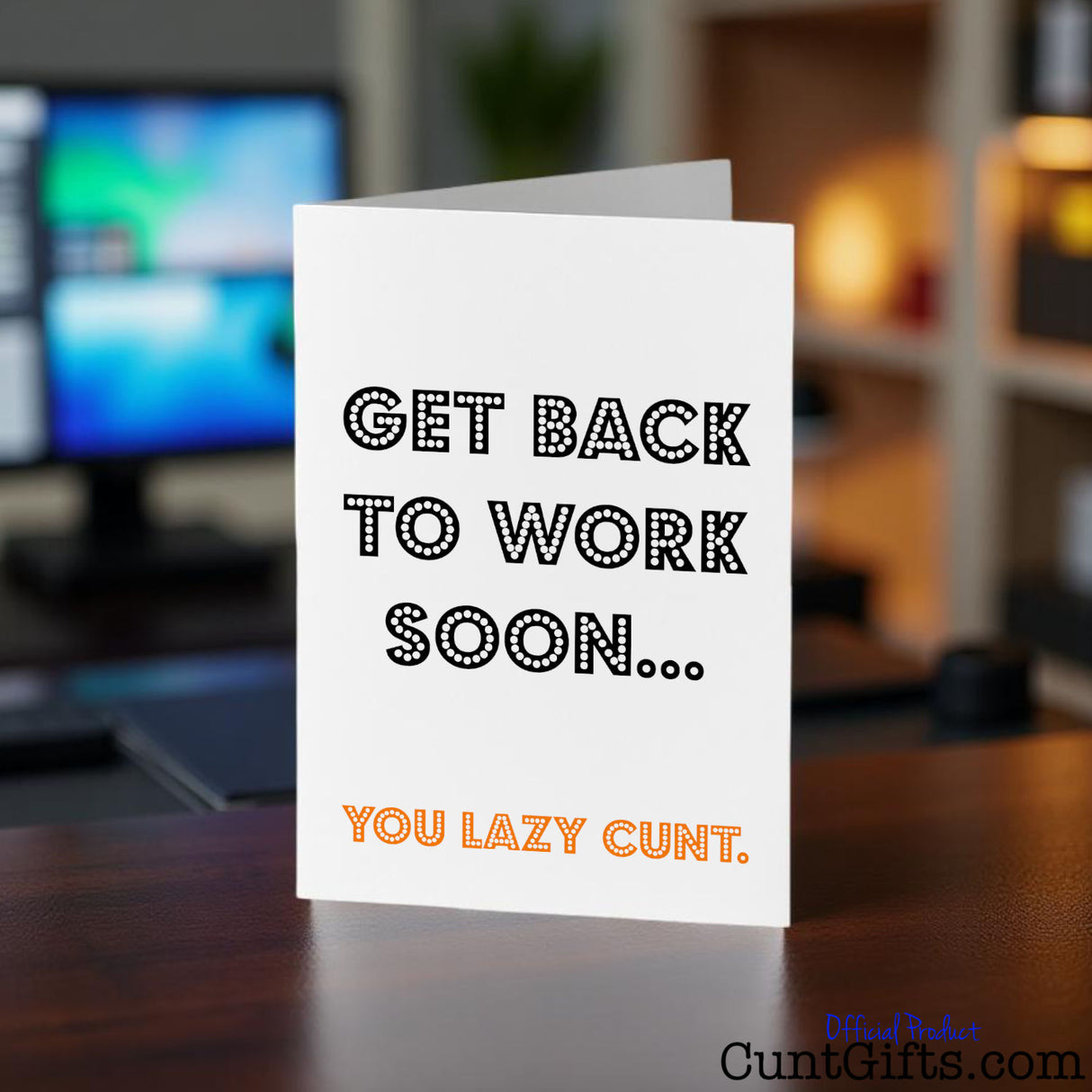 Card with text 'Get back to work soon... You lazy cunt.' on a desk with a blurred office background.