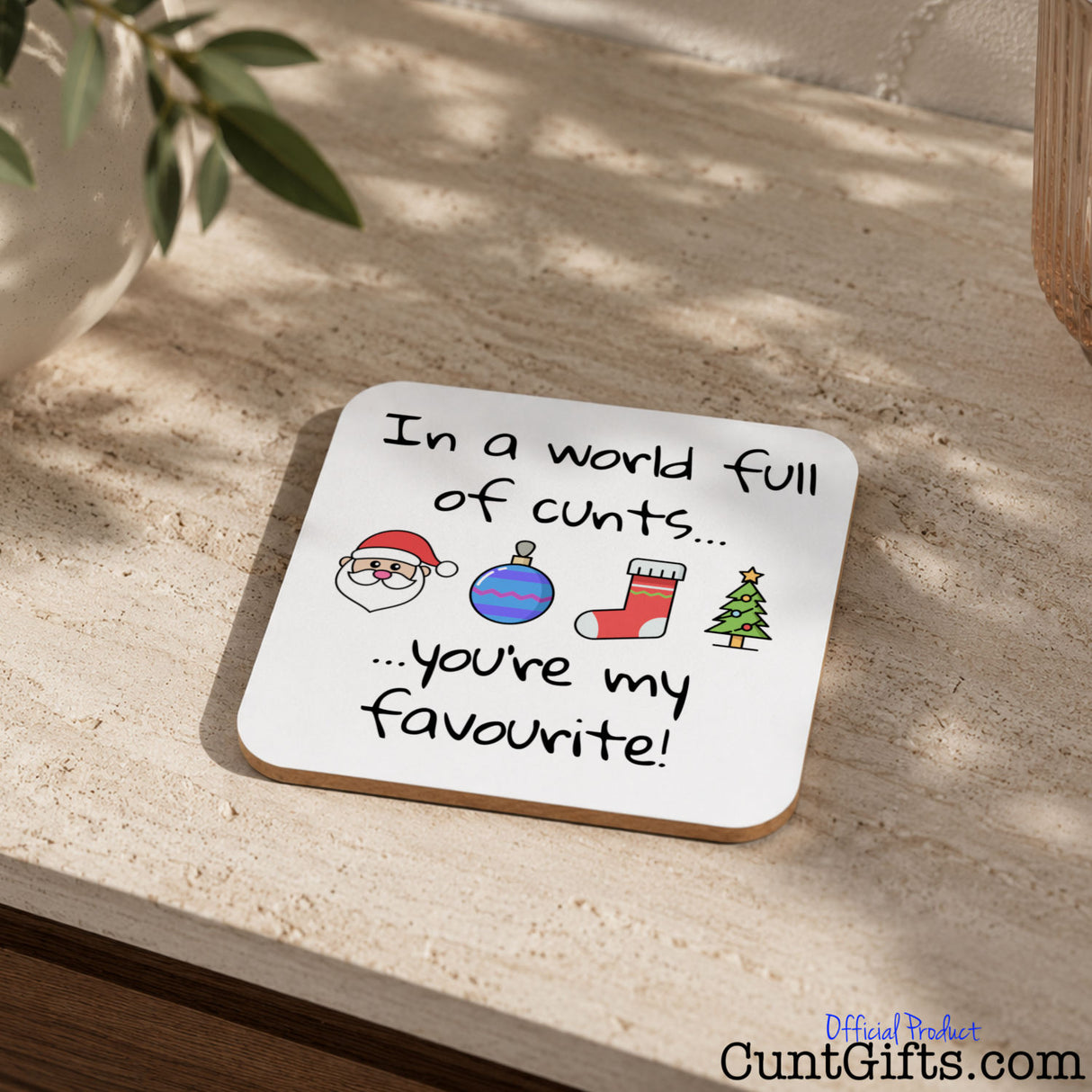 In A World Full Of Cunts You're My Favourite - Christmas Drink Coaster on table by plant and plant pot.