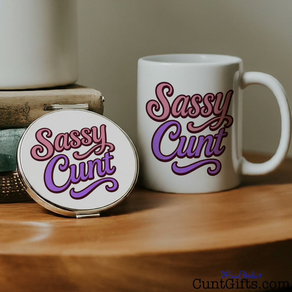 White mug and compact mirror with 'Sassy Cunt' text on a wooden surface.