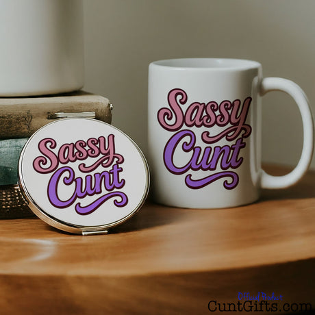White mug and compact mirror with 'Sassy Cunt' text on a wooden surface.