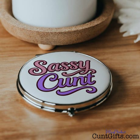 Compact mirror with 'Sassy Cunt' text on a wooden surface