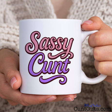 White mug with 'Sassy Cunt' text held by woman in a cardigan