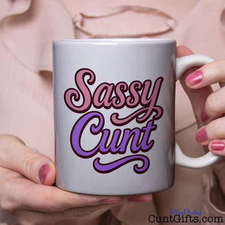 Mug with 'Sassy Cunt' text held by a person with pink blouse and nail polish.
