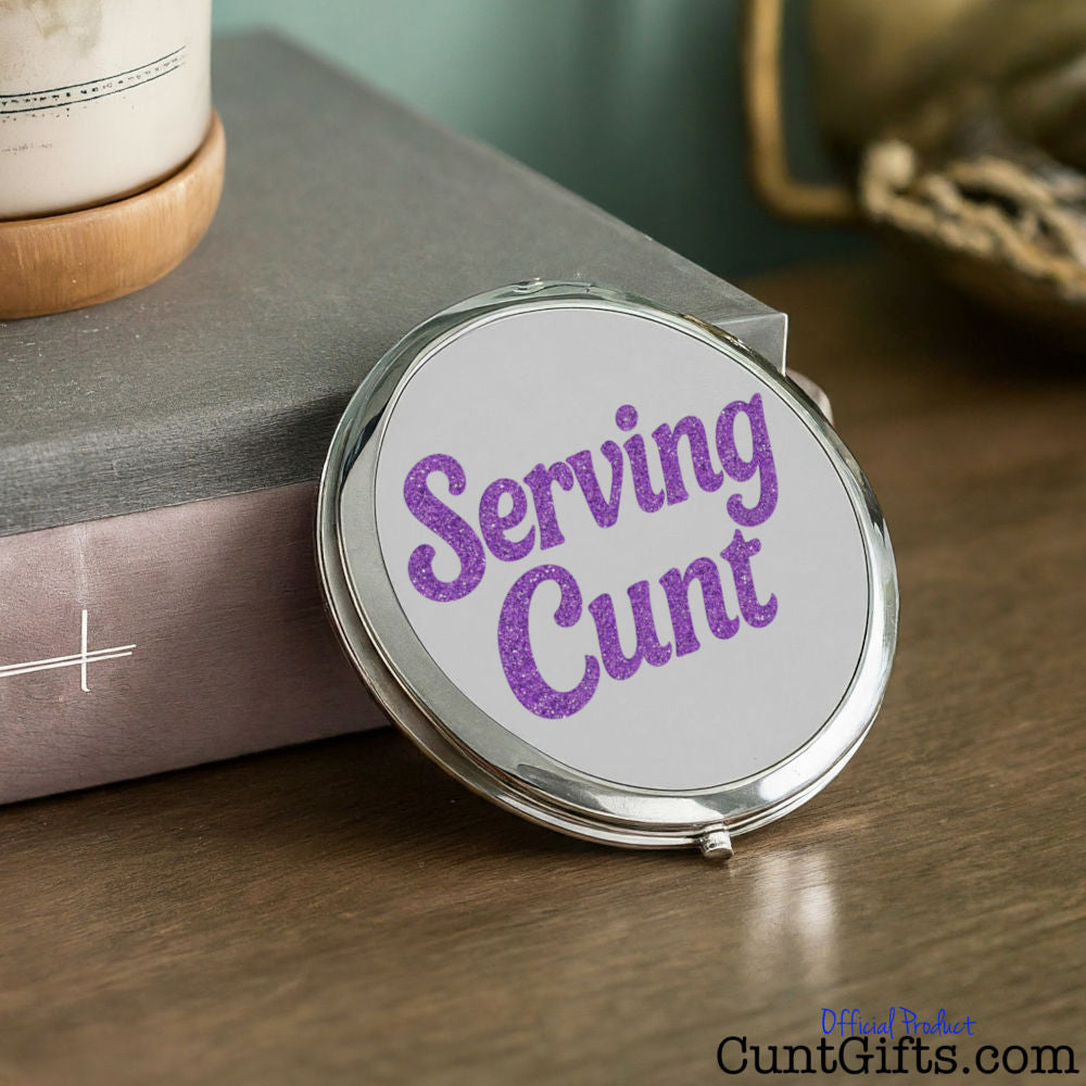 Compact mirror with 'Serving Cunt' text on a wooden surface
