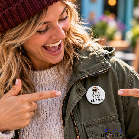 Smiling blonde woman pointing at her funny AI Cunt pin badge attached to a black jacket.