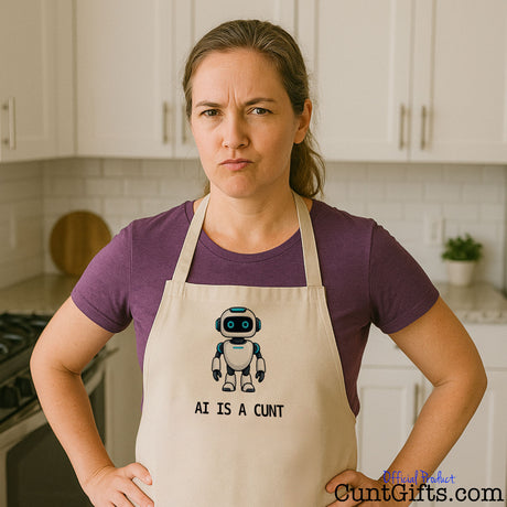 Woman wearing a rude AI Is a Cunt novelty apron with a cartoon robot design in a modern kitchen.