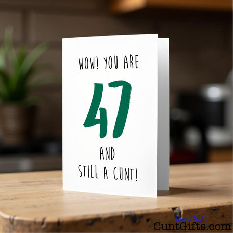 Card with text 'WOW! YOU ARE 47 AND STILL A CUNT!' on a wooden surface.