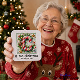 C is for Christmas and also for cunt - drink coaster held by laughing elderly woman in Christmas jumper by tree with fairy lights.