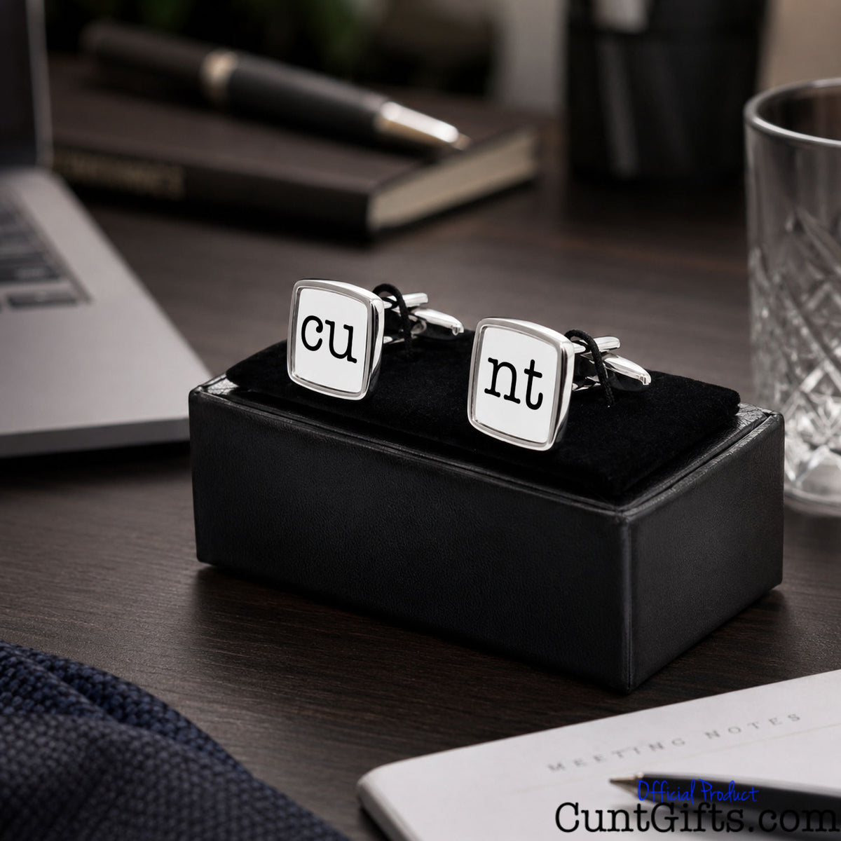 Cunt Cufflinks - CU and NT white design in presentation gift box on desk by laptop by pen, glass, notepad and book.