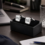 Cunt Cufflinks - CU and NT white design in presentation gift box on desk by laptop by pen, glass, notepad and book.