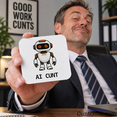 Smiling man in a suit holding up a funny AI Cunt drink coaster featuring an orange-eyed robot design.