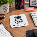 AI Is a Cunt novelty drink coaster featuring a cartoon robot on a wooden office desk beside a keyboard and notebook.