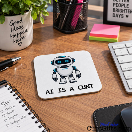 AI Is a Cunt novelty drink coaster featuring a cartoon robot on a wooden office desk beside a keyboard and notebook.