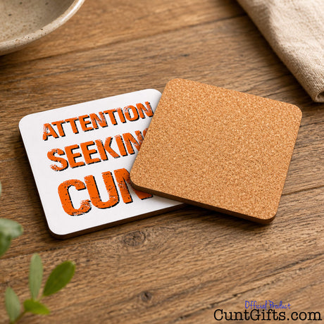 Attention Seeking Cunt - Drink Coaster showing both sides with cork backing on wooden table next to bowl and tea towel.