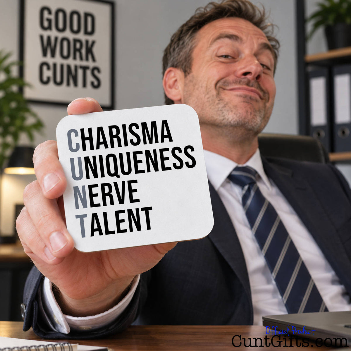 A man in a suit holds up a white square subtle cunt drinks coaster with black text reading 'CHARISMA UNIQUENESS NERVE TALENT' in a professional office setting.