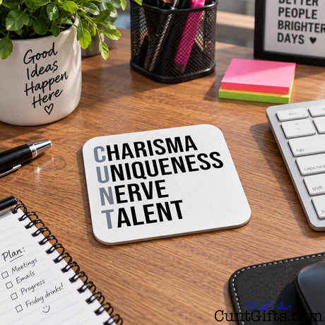  White square subtle cunt drinks coaster with black text reading 'CHARISMA UNIQUENESS NERVE TALENT' on a work desk with keyboard.