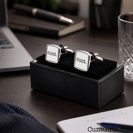 Cunt Cufflinks - white design in presentation gift box on office tablle next to laptop, pen and glass.