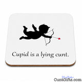 A square white coaster with rounded corners and a thin brown wood-look edge, featuring a black silhouette of Cupid with a bow and arrow and the text 'Cupid is a lying cunt.' on a white background.