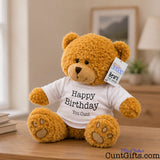 Happy Birthday You Cunt - Teddy Bear Plush sitting on bedroom sideboard by books and picture frame and lamp in background.
