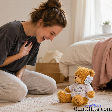 Happy Birthday You Cunt - Teddy Bear Plush on bedroom floor with woman laughing at it.