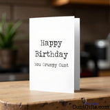 Happy Birthday You Grumpy Cunt birthday card on a wooden surface with a blurred background