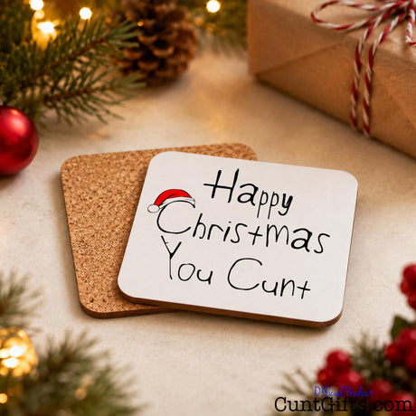 Happy Christmas You Cunt drink coaster showing both sides with cork 
 backing by branches, baubles and a wrapped gift.