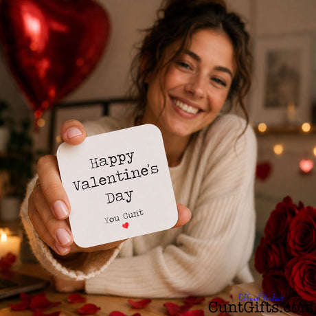 Happy Valentines Day You Cunt - drink coaster held by smiling woman with roses and heart balloon.
