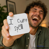 A man in a green shirt holds up a white drinks coaster that reads 'I cunt spell' in black handwriting, with a warm indoor background and a visible 'CuntGifts.com' watermark in the lower right corner.