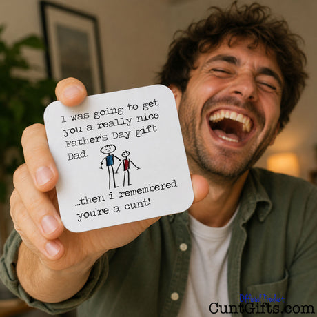 I remembered you're a cunt Dad -  Father's Day Drink Coaster held by laughing man in lounge by lamp and picture frame. 