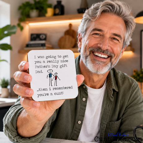 I remembered you're a cunt Dad -  Father's Day Drink Coaster held by older dad with grey beard in front of shelves in lounge.