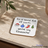 In A World Full Of Cunts You're My Favourite - Christmas Drink Coaster on table by plant and plant pot.