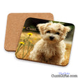 Two square cork drink coasters shown on a white background, one plain cork and one printed with a photo of a fluffy cream-colored dog sitting in grass with yellow flowers and the word 'Cunt.' on the coaster.