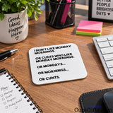 A square white coaster with rounded corners featuring black text that reads 'I DON'T LIKE MONDAY MORNINGS. OR CUNTS WHO LIKE MONDAY MORNINGS.