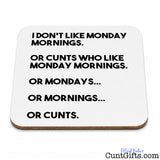 A square whitedrinks coaster with rounded corners and a thin brown edge, printed with black text that reads, 'I DON'T LIKE MONDAY MORNINGS. OR CUNTS WHO LIKE MONDAY MORNINGS.
