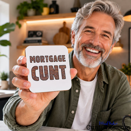 A smiling older man with gray hair and a beard holds up a square white sign that reads “MORTGAGE CUNT” in large brown outlined letters. He is wearing an olive green shirt over a white undershirt in a warm indoor setting with shelves and plants in the background.