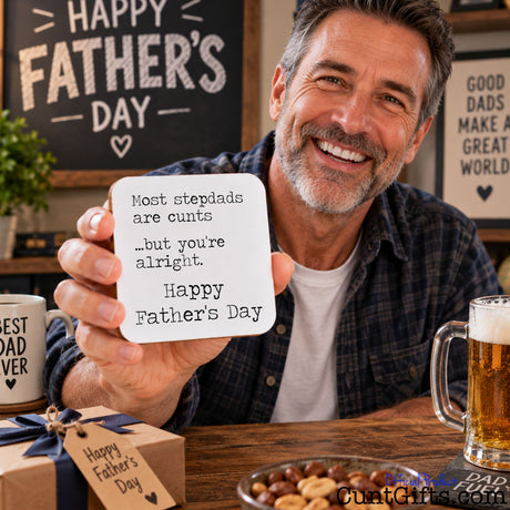 A smiling man in a plaid shirt holds up a square white card with black text that says, 'Most stepdads are cunts  ...but you're alright - Happy Father's Day'