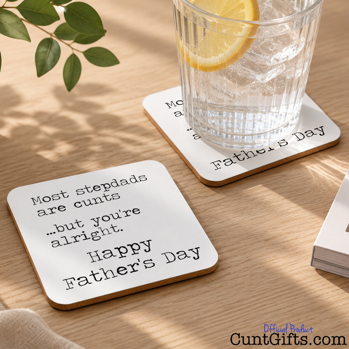 A square white Father's Day coaster on table with a glass of lemon water, with black printed text reading 'Most stepdads are cunts  ...but you're alright - Happy Father's Day'.