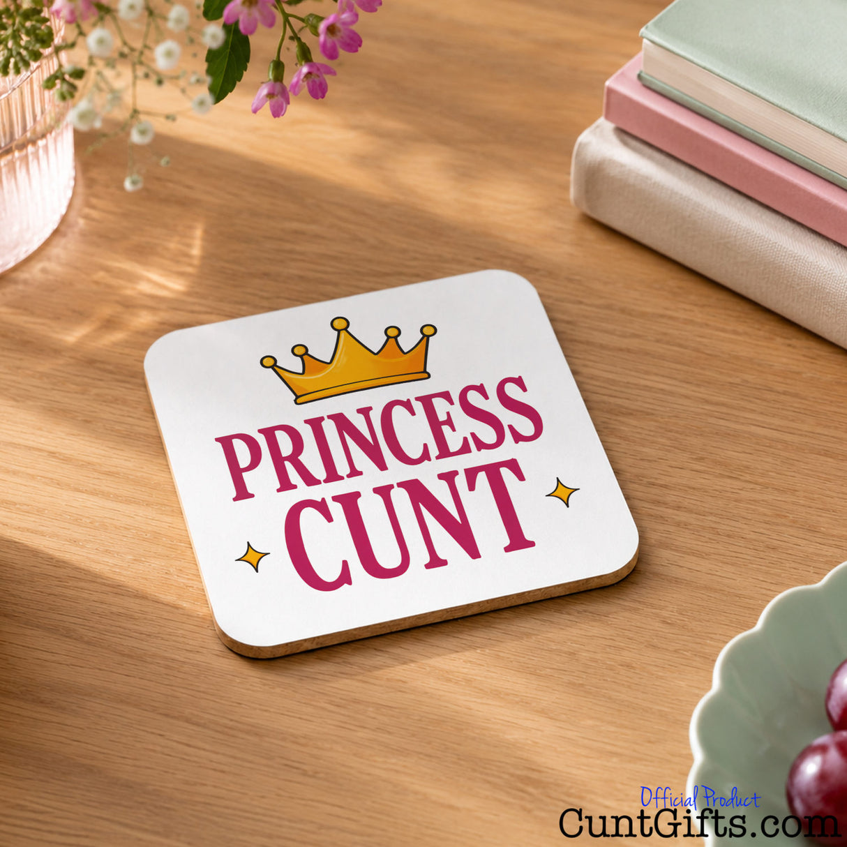 Princess Cunt Drink Coaster on table with books flowers and grapes