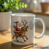 "Get Off Me You Fat Cunt" - Christmas Mug featuring Santa and Rudolph on table with plant