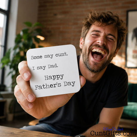 Some say cunt I say Dad - Father's Day Drink Coaster held by laughing man in studio with plant in background.