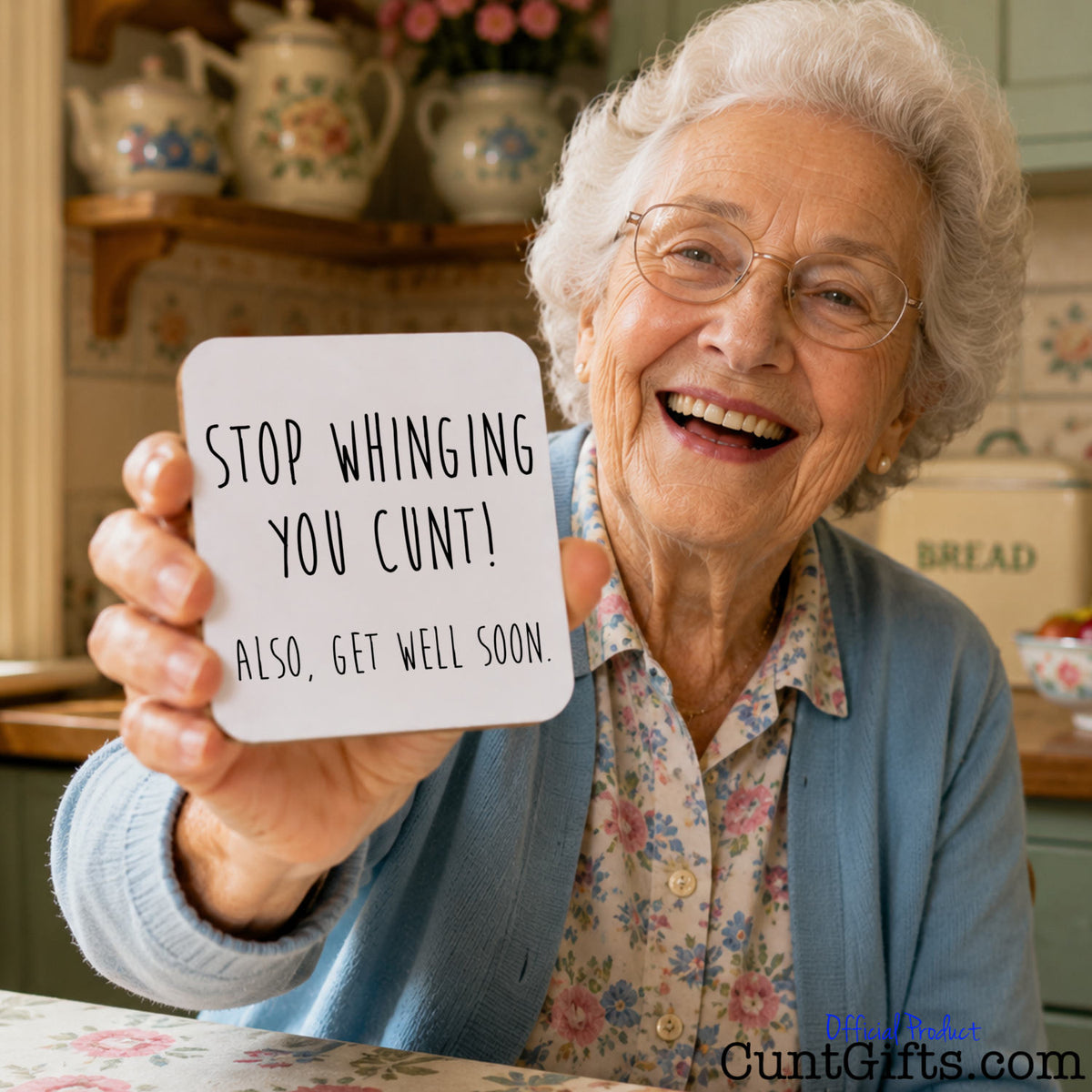 An elderly woman with white hair and glasses smiles while holding up a white square drinks coaster that reads, 'STOP WHINGING YOU CUNT! ALSO, GET WELL SOON.' in black handwritten-style text.
