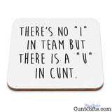 A square white coaster with rounded corners and a thin brown wood edge, printed with the humorous phrase 'THERE'S NO "I" IN TEAM BUT THERE IS A "U" IN CUNT.' in black handwritten-style lettering.