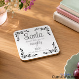 You are not naughty or nice you're a cunt - Christmas Drinks Coaster on wooden table next to books, flowers and grape bowl.