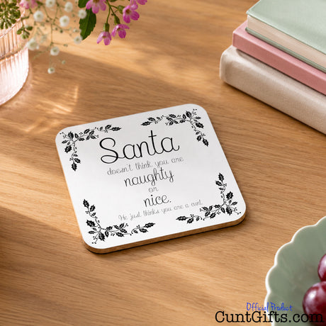 You are not naughty or nice you're a cunt - Christmas Drinks Coaster on wooden table next to books, flowers and grape bowl.